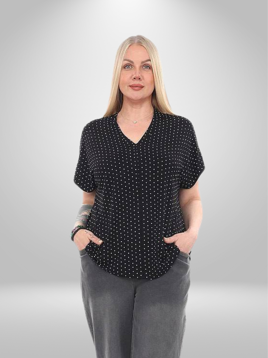 A plus-size model wearing a black polka dot blouse (sizes 20-26), featuring a V-neckline and breathable lightweight fabric, paired with grey trousers.